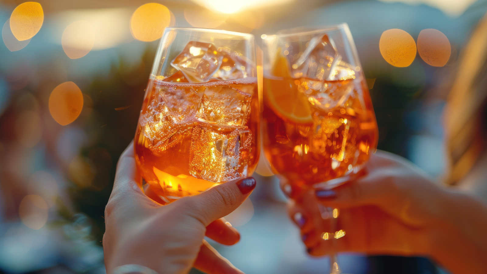 Zwei weibliche Hände toasten sich mit einem Aperol Spritz zu